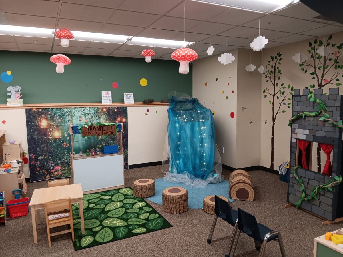 colorful classroom decorated with fantasy elements, including fake mushrooms on the ceiling, tree stumps, a blue cave, a castle, and woodland themed rugs and furniture.