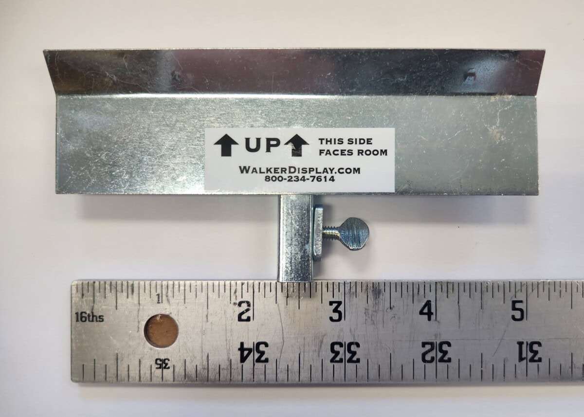 metal wall hanger with adjustment screw and label, placed above a ruler showing a length of approximately 5 inches.