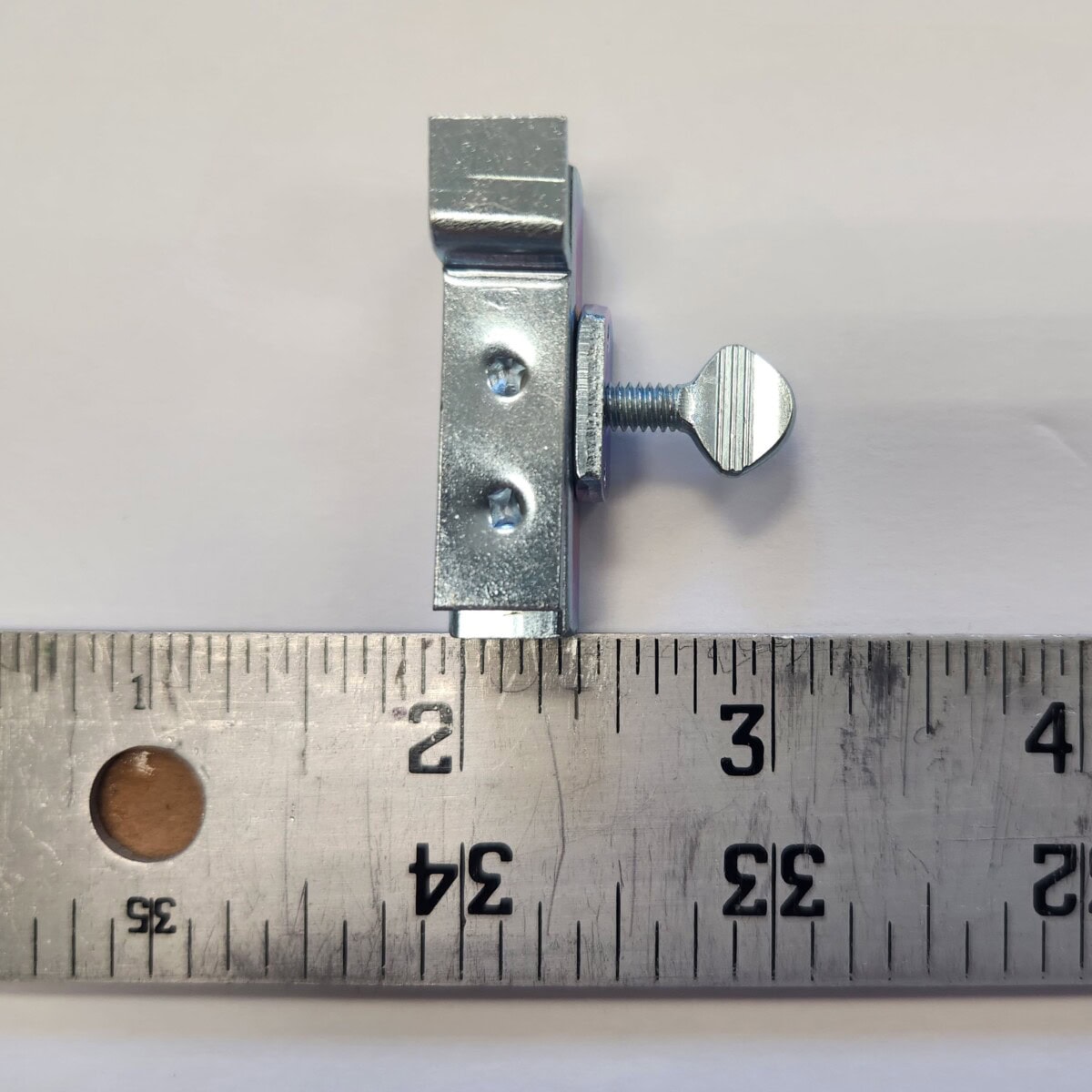 a metal clamp with a screw sits on a white surface next to a metal ruler, showing the clamp is about 2 inches in length.