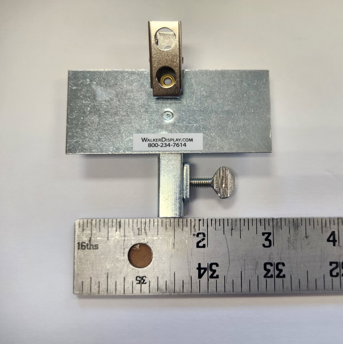 metal picture hanging hardware and ruler on a white surface, with “walker display” label and a phone number visible on the hardware.