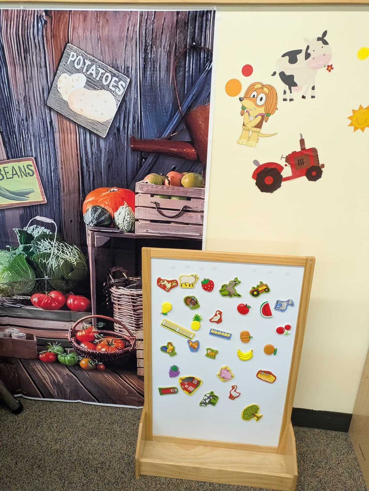 a classroom corner with a vegetable themed backdrop, food and farm stickers on the wall, and a magnet board displaying colorful magnets shaped like foods and farm items.